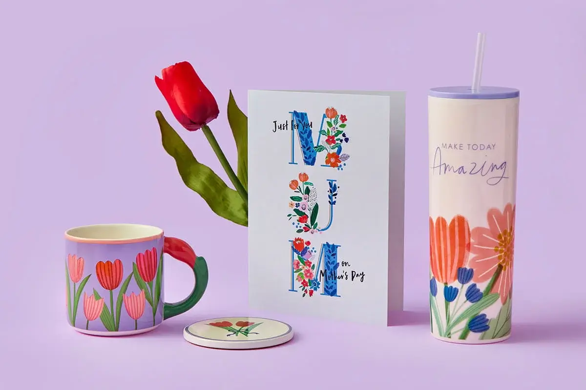 A floral Mother’s Day set featuring a pastel jug filled with pink and orange flowers, a butterfly‑decorated Grandma mug, and a garden‑themed Mum card arranged on a pastel purple background.